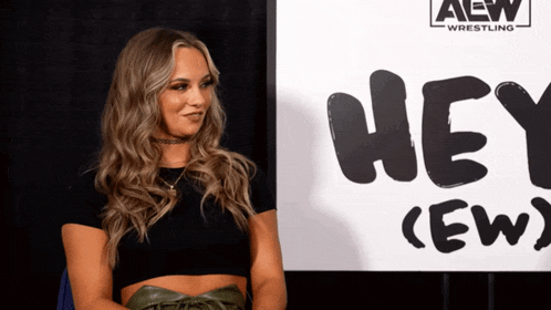 a woman sitting in front of a sign that says hey crew