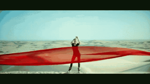 a woman in a red dress is standing in the desert holding a red cloth