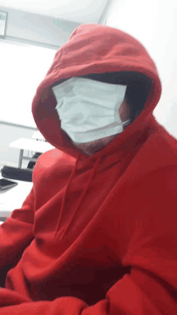 a person wearing a red hoodie and a white mask on their face