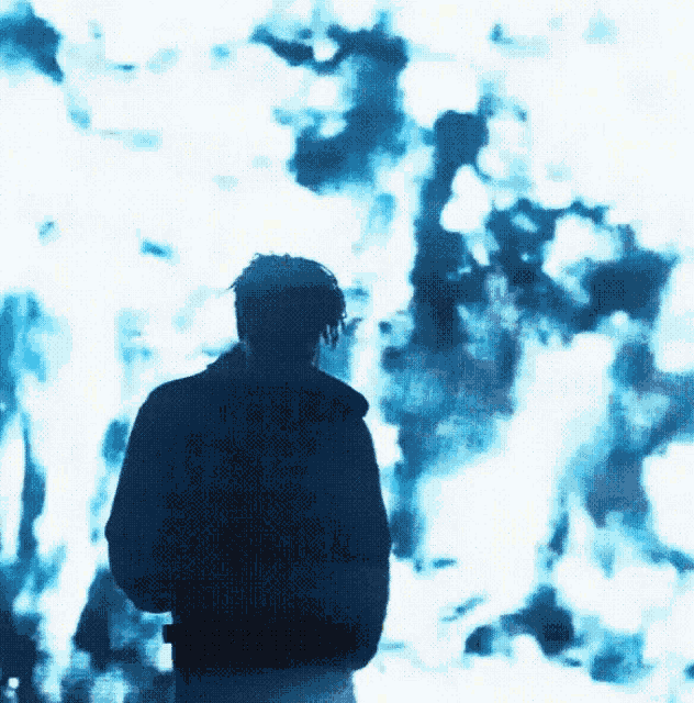 a man in a black jacket stands in front of a blue fire