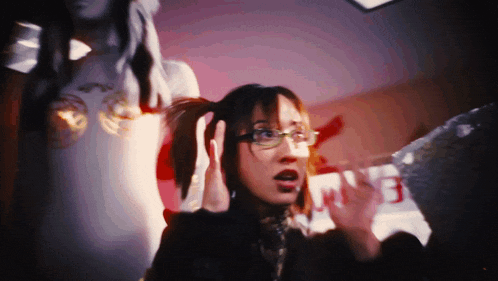 a woman wearing glasses holds her hands to her ears in front of a sign that says ' nb ' on it