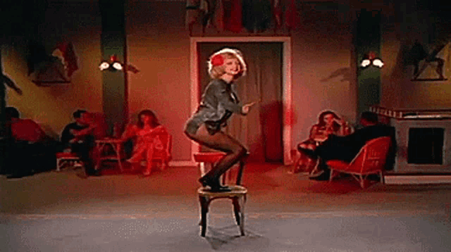 a woman is standing on a stool in a room with people sitting in chairs .