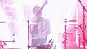 a man is playing drums on a stage with a pink background .
