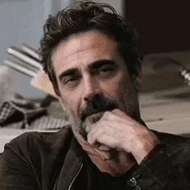 a man with a beard and glasses is holding his hand to his chin and looking at the camera .