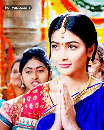 a woman in a blue saree is praying with her hands folded in front of her face .