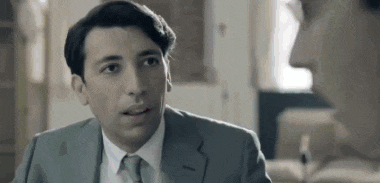 a man in a suit and tie is looking at another man in a room .
