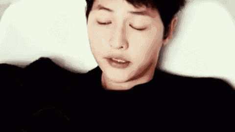 a young man is laying in bed with his eyes closed .