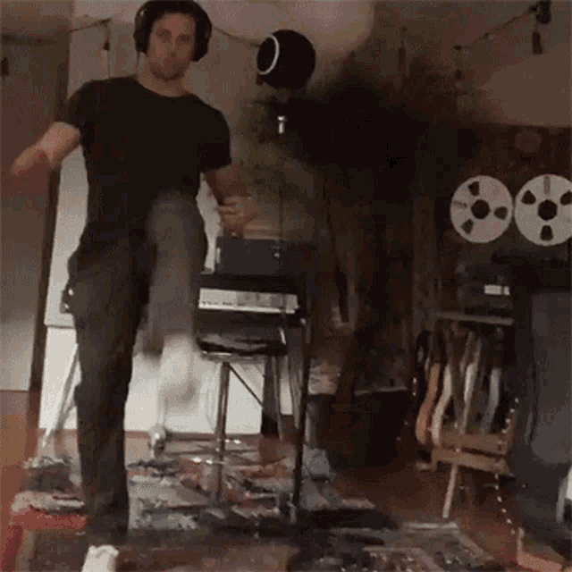 a man wearing headphones is playing a guitar in a room with tape reels on the floor .