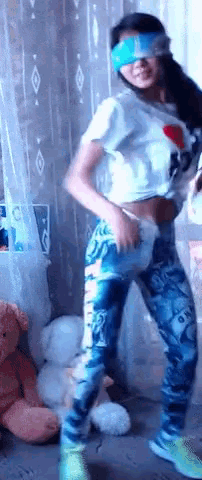 a girl wearing a blue blindfold is dancing in front of a teddy bear
