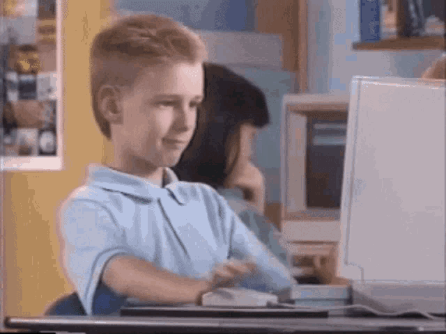 a young boy in a blue shirt is sitting at a desk in front of a computer .