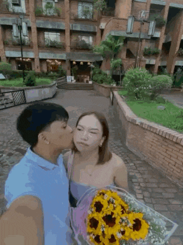 a man is kissing a woman on the cheek while she holds a bouquet of flowers .