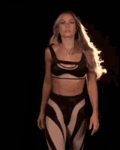 a woman in a black crop top and matching pants has a necklace with the letter m on it