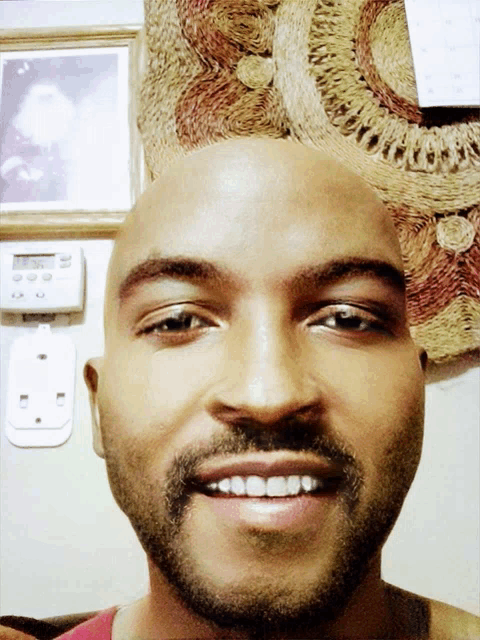 a bald man with a beard is smiling in front of a wall clock that says the time is 4:20