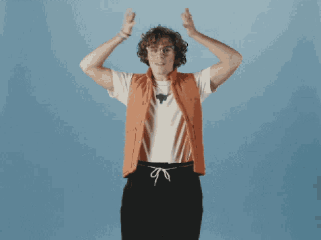 a man wearing an orange vest and a white t-shirt holds his hands on his head