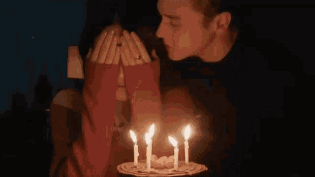 a man is kissing a woman on the cheek in front of a birthday cake with lit candles .