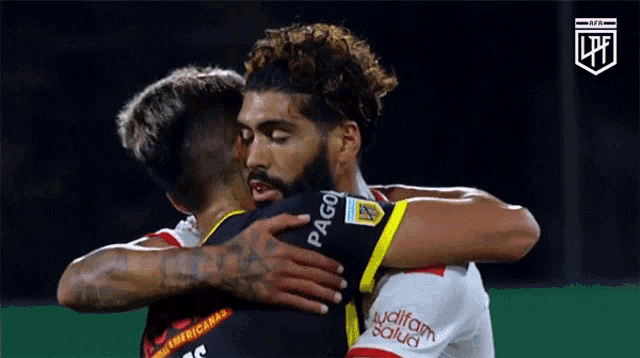 two soccer players hugging each other with one wearing a jersey that says pago