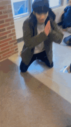 a man in a green jacket is kneeling on the floor with his hands folded in prayer .