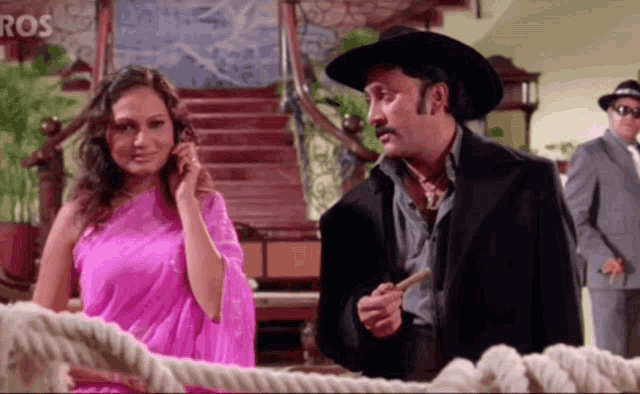 a woman in a pink saree talks on a cell phone while a man in a cowboy hat looks on