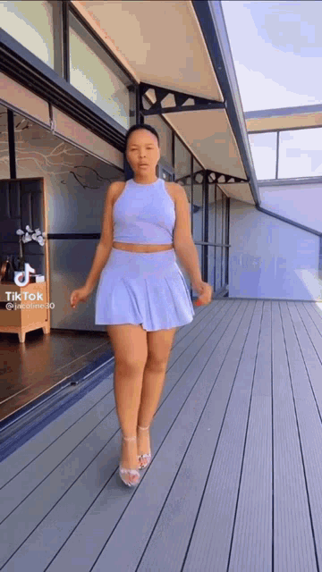 a woman in a white crop top and skirt is standing on a wooden deck in front of a building .