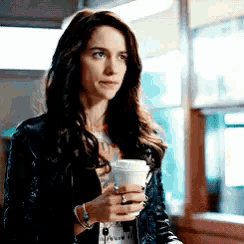 a woman in a black jacket is holding a cup of coffee in her hand