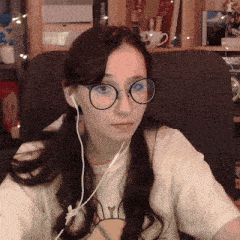 a woman wearing glasses and ear buds is sitting in a chair