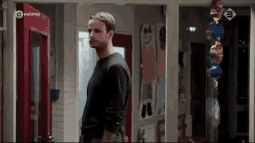 a man in a black shirt is standing in a hallway looking at something .