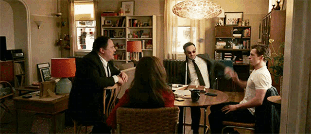 a group of people are sitting around a table in a living room having a conversation .