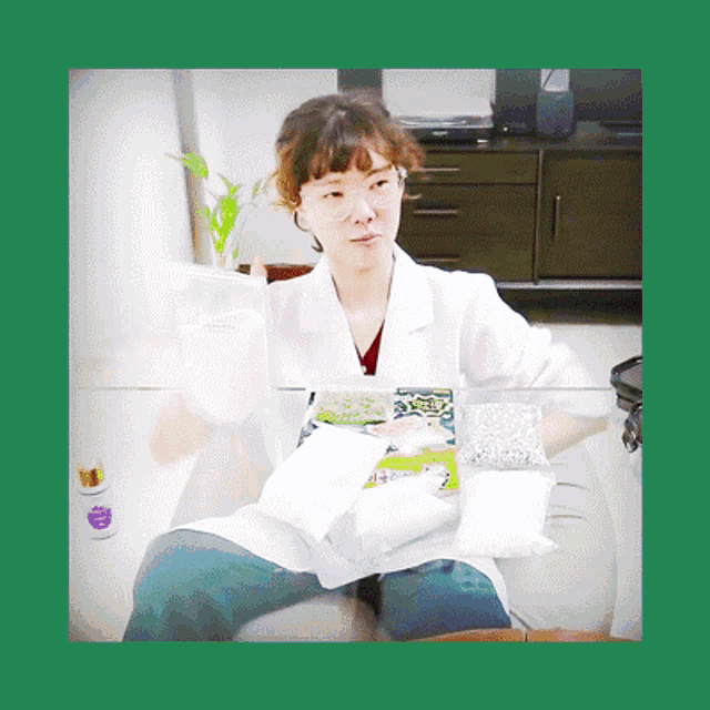 a woman in a lab coat is sitting at a table with a bottle of purple liquid in front of her