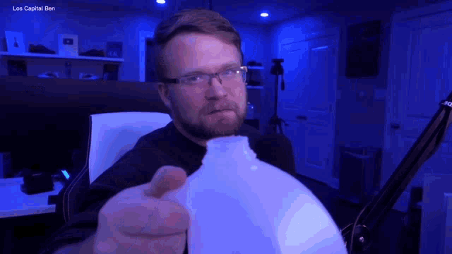a man with glasses is holding a gallon of milk in front of a blue background that says los capital ben on it