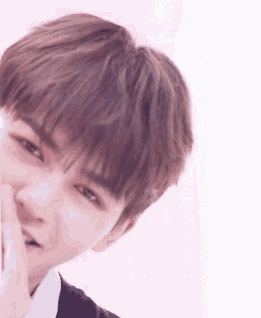 a close up of a young man 's face with a pink background and a hand on his face .