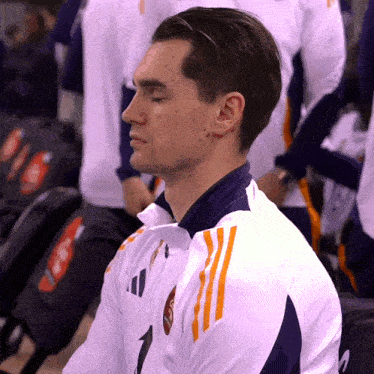 a man wearing a white jacket with orange stripes and the number 1 on it sits with his eyes closed
