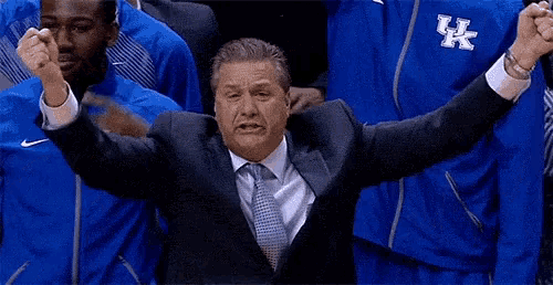 a man in a suit and tie is screaming in front of a group of players wearing blue jackets with uk on them