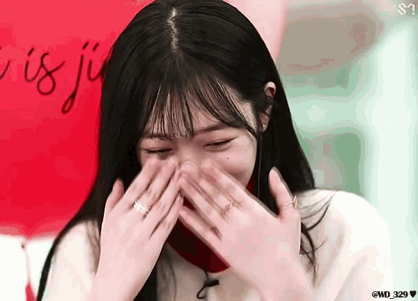 a woman covering her face with her hands in front of a red sign that says ' i is ju '