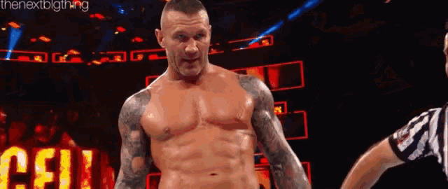 a shirtless wrestler is standing next to a referee .