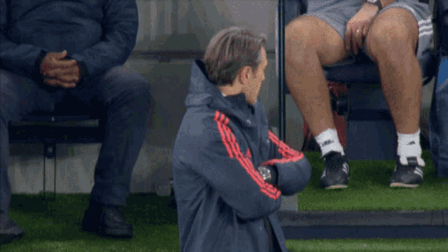 a man wearing an adidas jacket is sitting on the grass