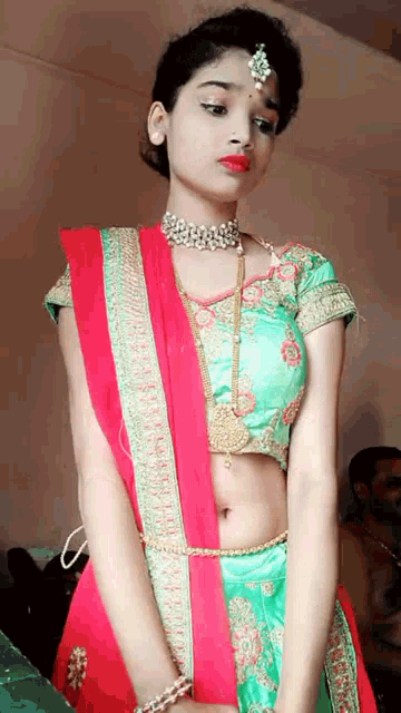 a woman wearing a green top and a red skirt is standing in front of a wall .