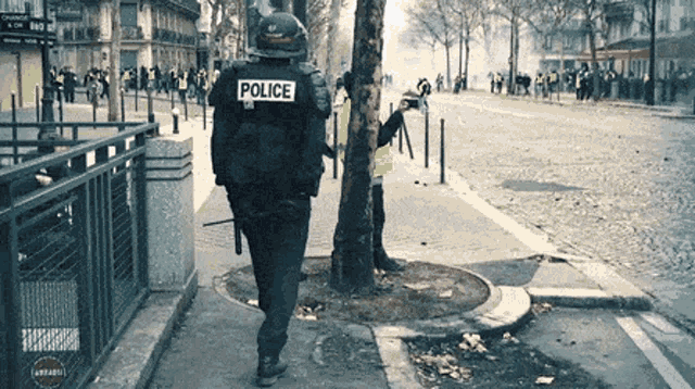 a police officer walking down a street with a crowd in the background