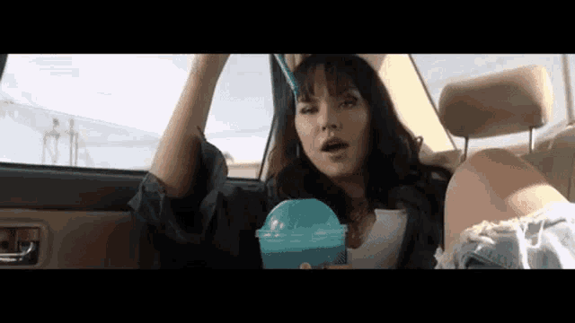 a woman is sitting in the back seat of a car drinking from a blue cup with a straw .