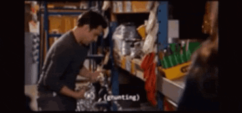 a man is standing in front of a shelf in a warehouse and talking to another man .