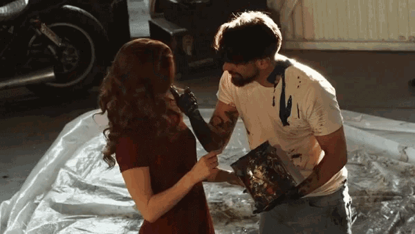 a man and a woman are standing next to each other and the man has paint on his shirt