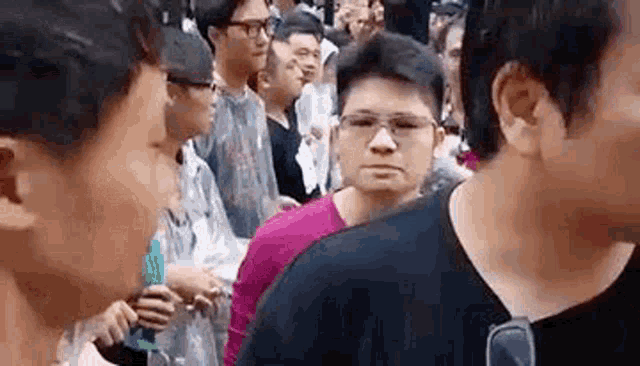 a group of people are standing in a crowd and one of them is wearing glasses and a pink shirt .