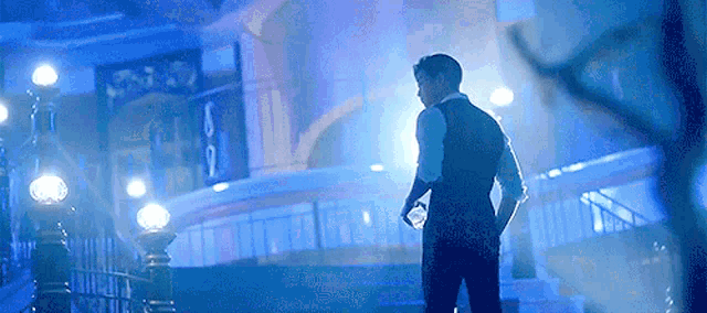 a man in a suit is standing in front of a building in a dark room holding a bottle of water .