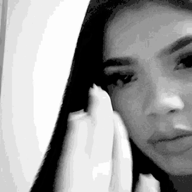 a black and white photo of a woman wiping her face with a cloth .