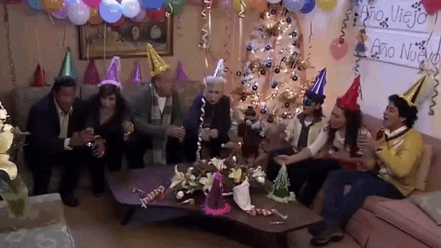 a group of people wearing party hats sit in front of a sign that says " ano nuevo "
