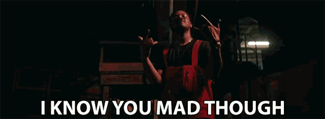 a man in red overalls is standing in a dark room with the words i know you mad though behind him