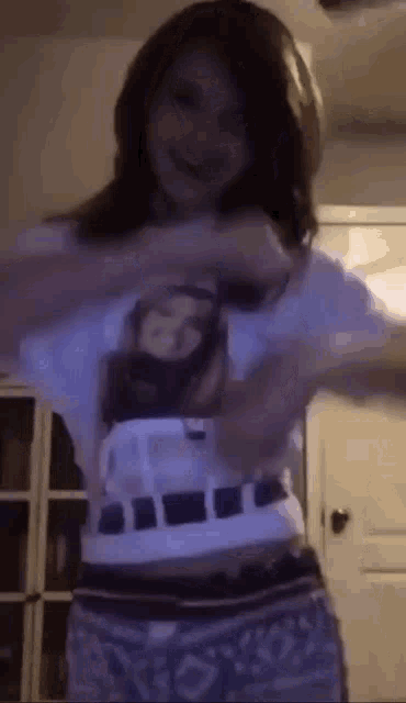 a young girl is taking off her shirt and dancing in a room .