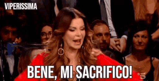 a woman in a red dress is sitting in front of a crowd and says bene , mi sacrifico !