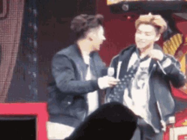 two men are standing next to each other on a stage and one is adjusting his tie .