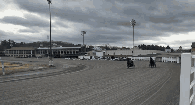 two horse drawn carriages on a dirt track with a building in the background