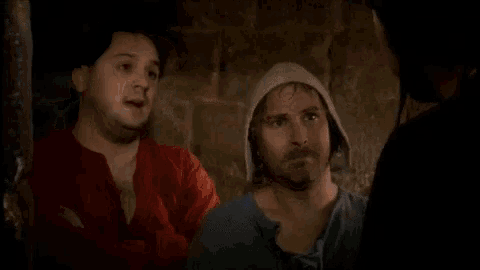 a group of men are standing next to each other in a dark room . one of the men is wearing a hood .
